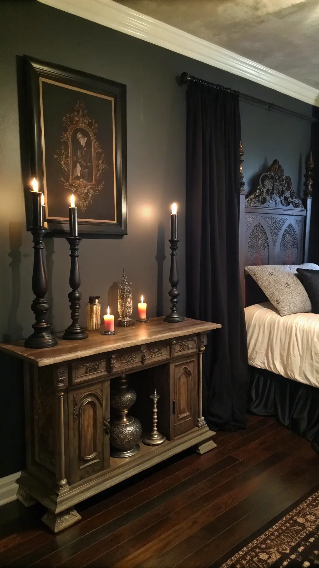 Gothic-themed bedroom with antique altar table as headboard, black candles, vintage mercury glass artifacts, heavy silk drapes on dark hardwood floors, and asymmetrical artwork on charcoal walls