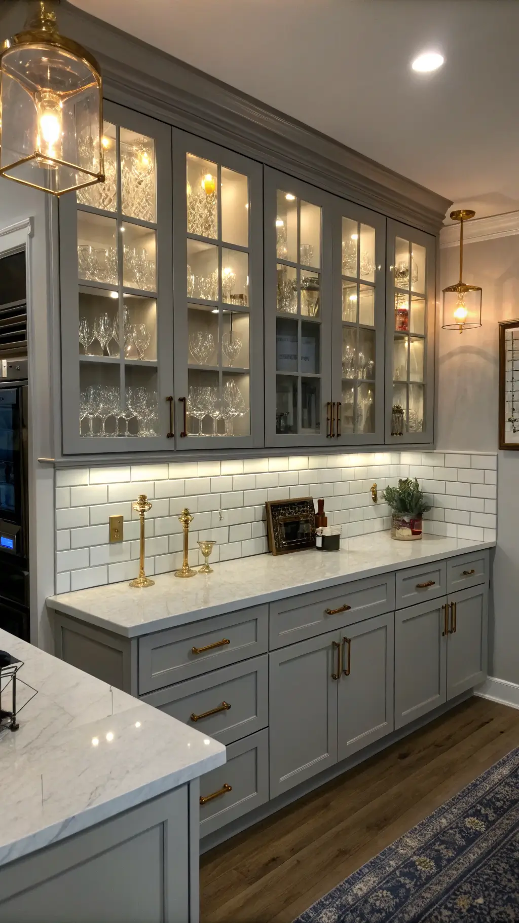 Transitional kitchen at dusk with Galaxy Horizon light gray cabinets, double-height upper cabinets with glass fronts, brass hardware, white subway tile backsplash, and charcoal center island; shot from above island.