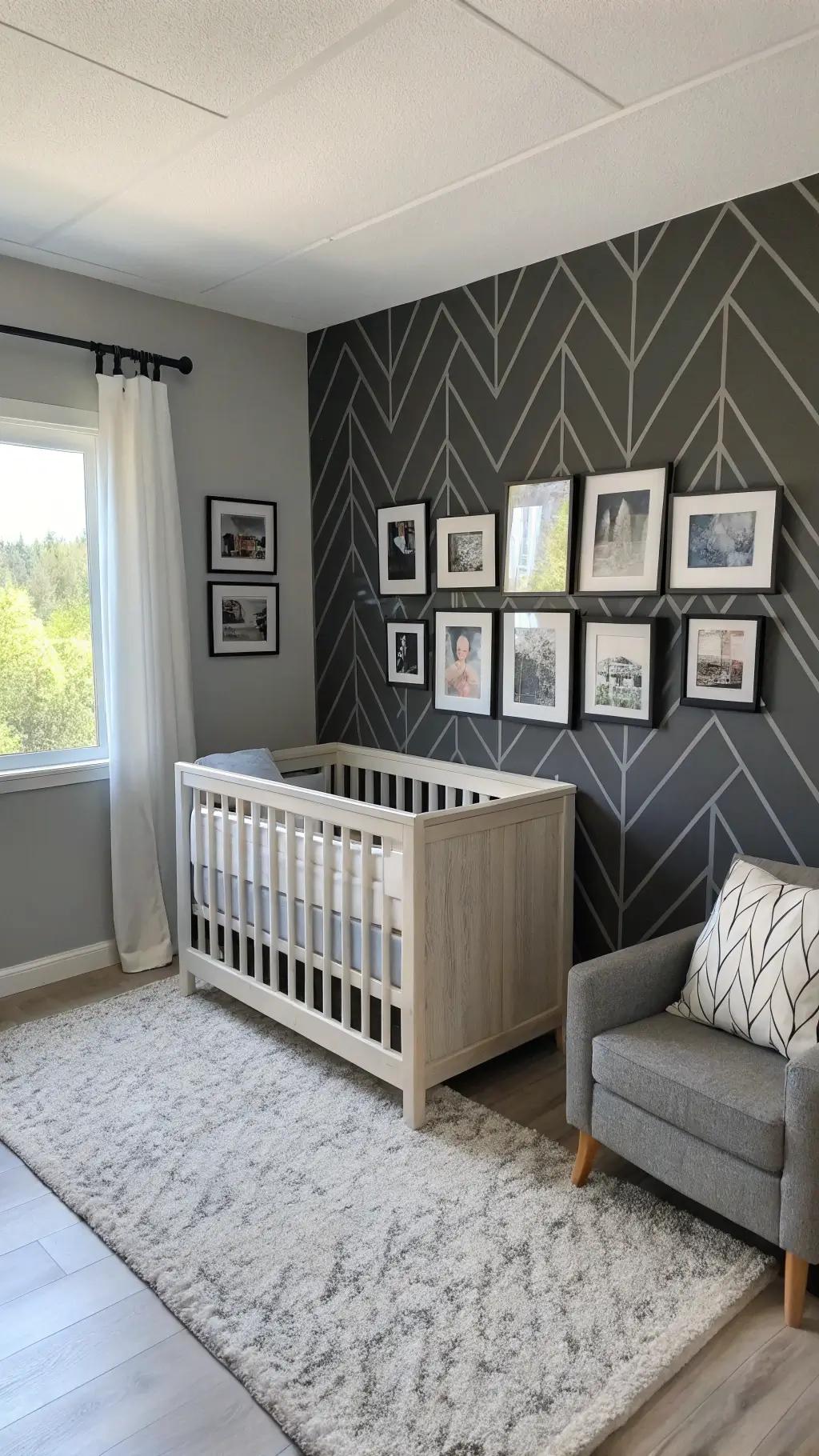 Minimalist nursery with charcoal geometric accent wall, light grey crib and glider, black and white photography wall, textured rug, modern black mobile, under natural window light and fill lighting.