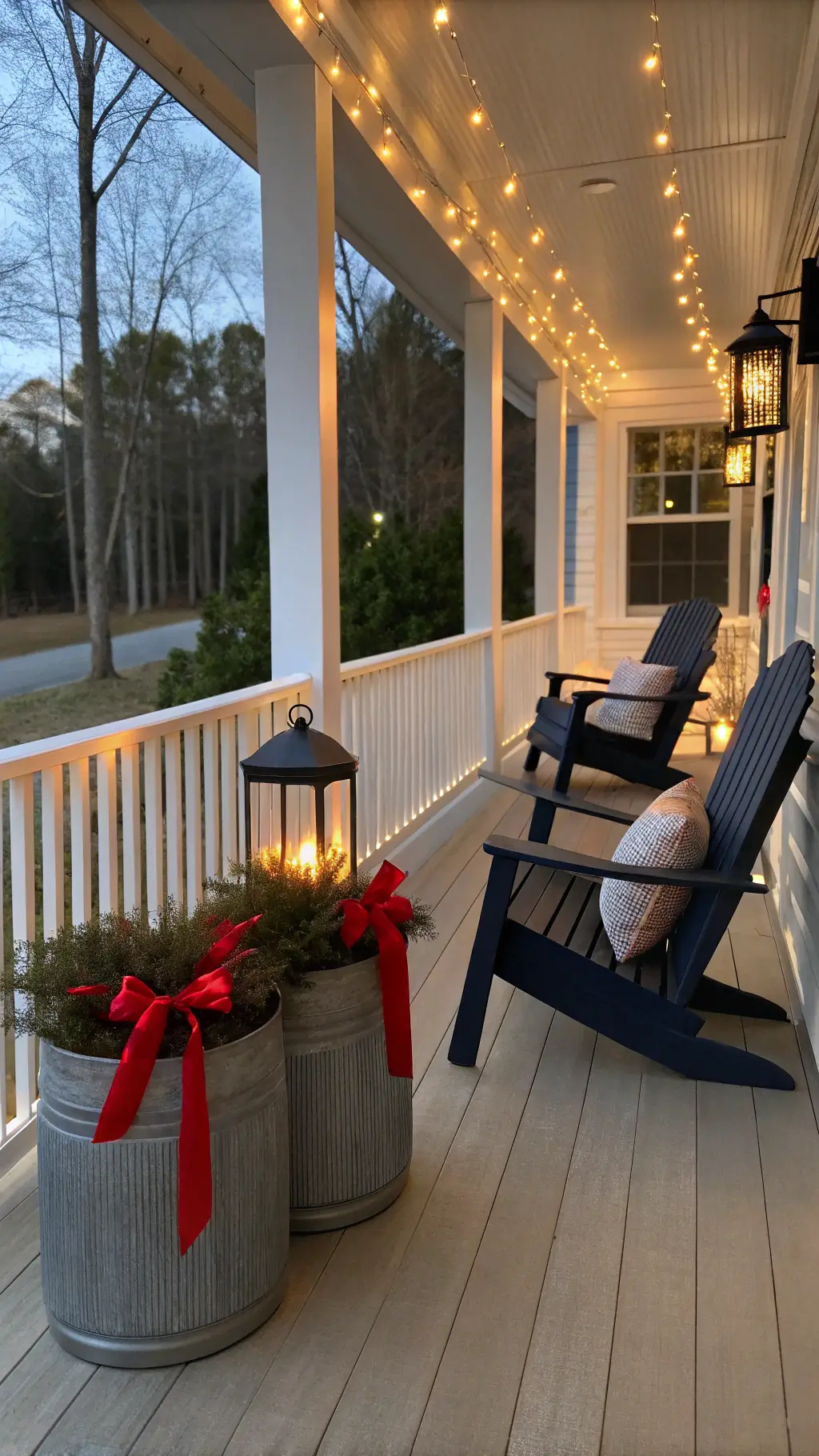 Modern wraparound porch at dusk with white LED string lights, black Adirondack chairs with navy cushions, oversized planters with red geraniums, and copper lanterns for ambient lighting.