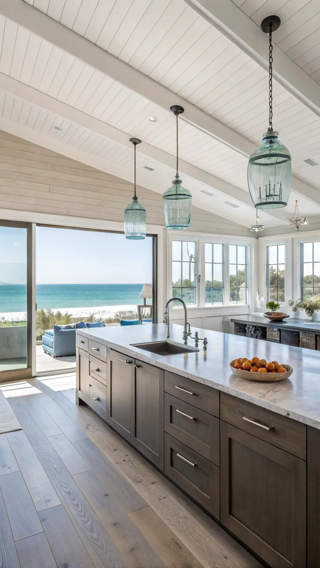 Bright coastal modern kitchen with dark taupe flat-panel cabinets, quartzite counters, bleached oak floors, and large windows offering ocean views.