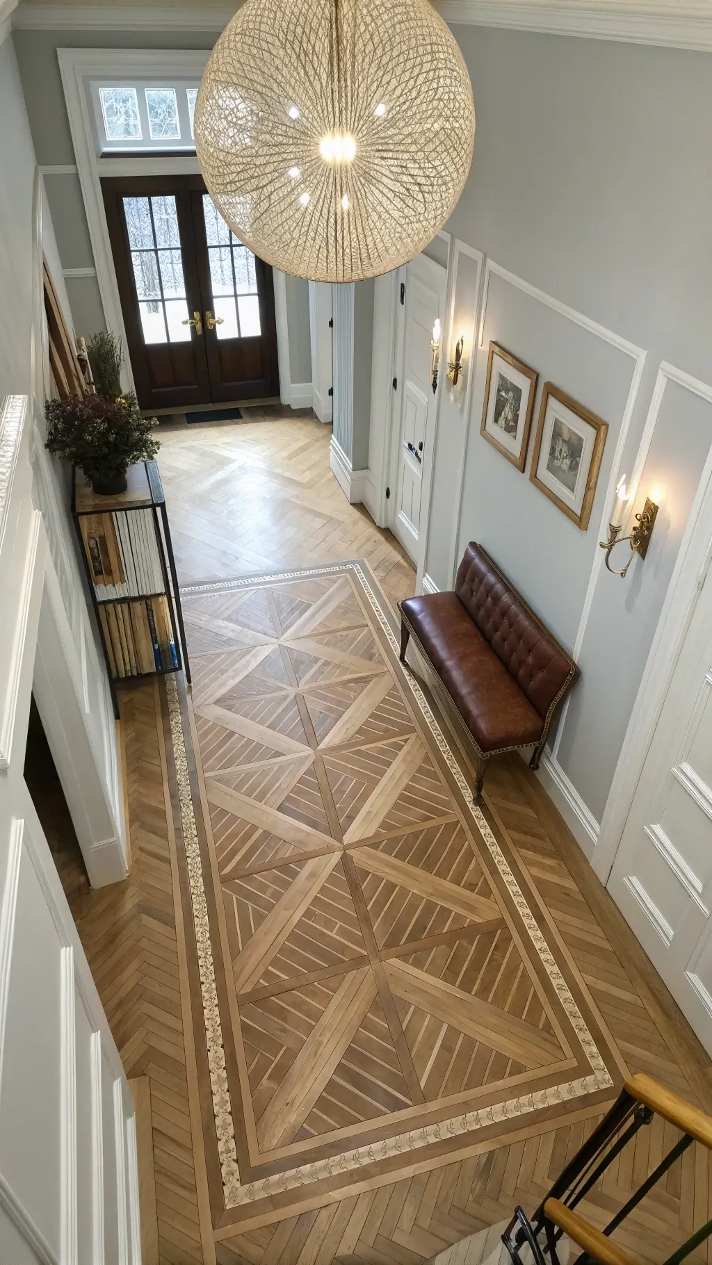 Bird's eye view of a 16ft hallway intersection with restored pine floors in chevron pattern, brass inlay, dove gray lime wash walls, oversized woven pendant light, and a leather bench with steel frame.