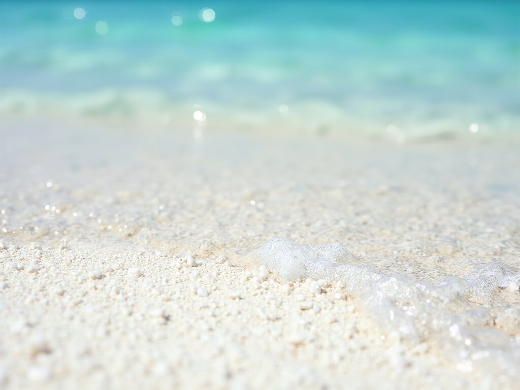 Close-up of white sandy beach texture with fine quartz grains, crystal clear water with aquamarine reflections, gentle waves and diffused sunlight highlighting the geological characteristics